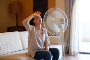 Woman feeling hot and trying to refresh in summertime heat in front of fan